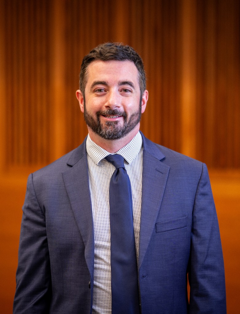 James headshot, man with dark hair and beard dressed in blue suit and